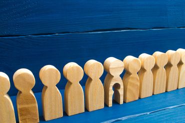 Foto: Holzfiguren in einer Reihe, eine hat ein ausgeschnittenes Kind